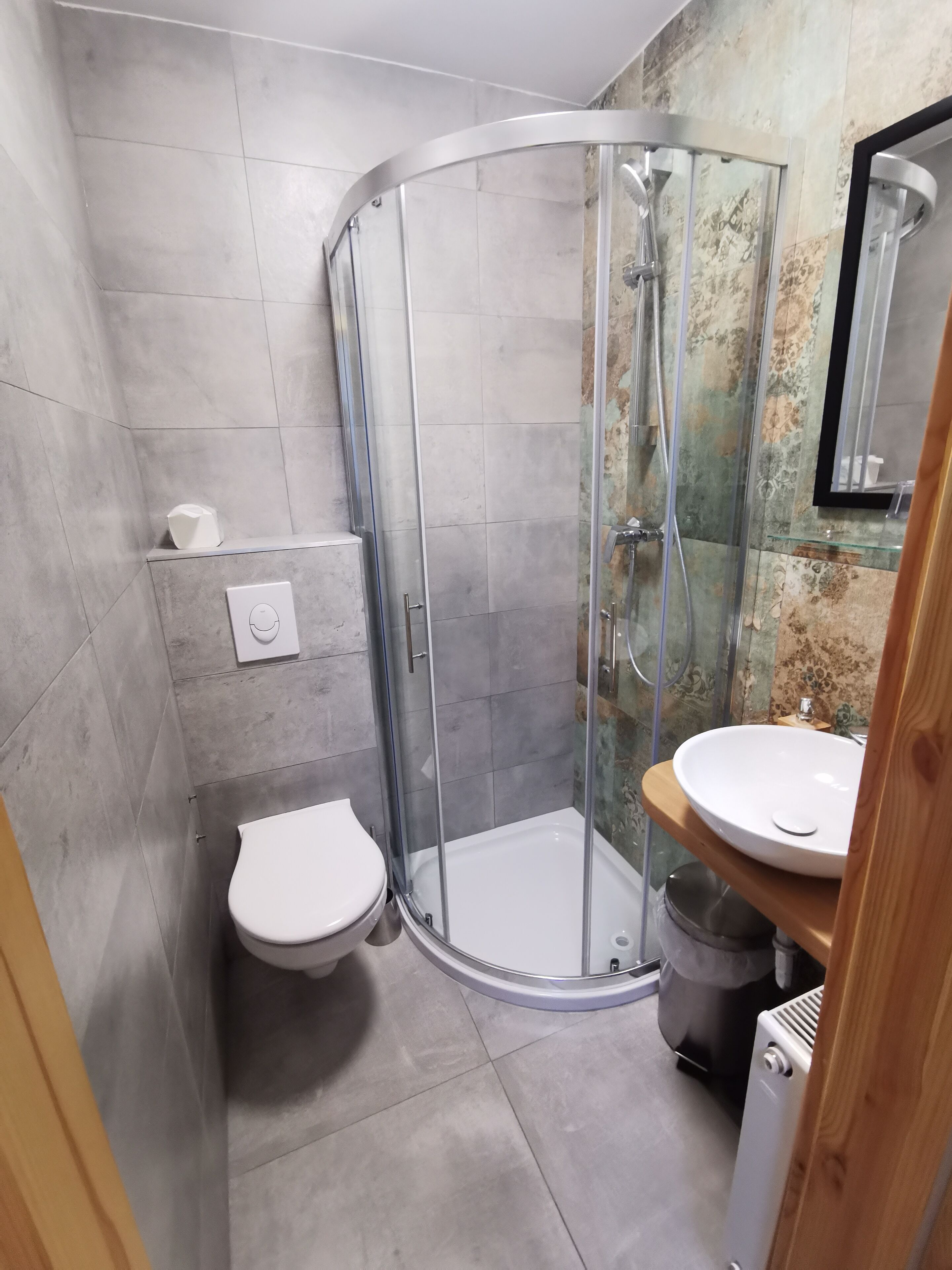 Un baño con ducha envuelta en vidrio, inodoro blanco y tocador de madera con lavamanos.