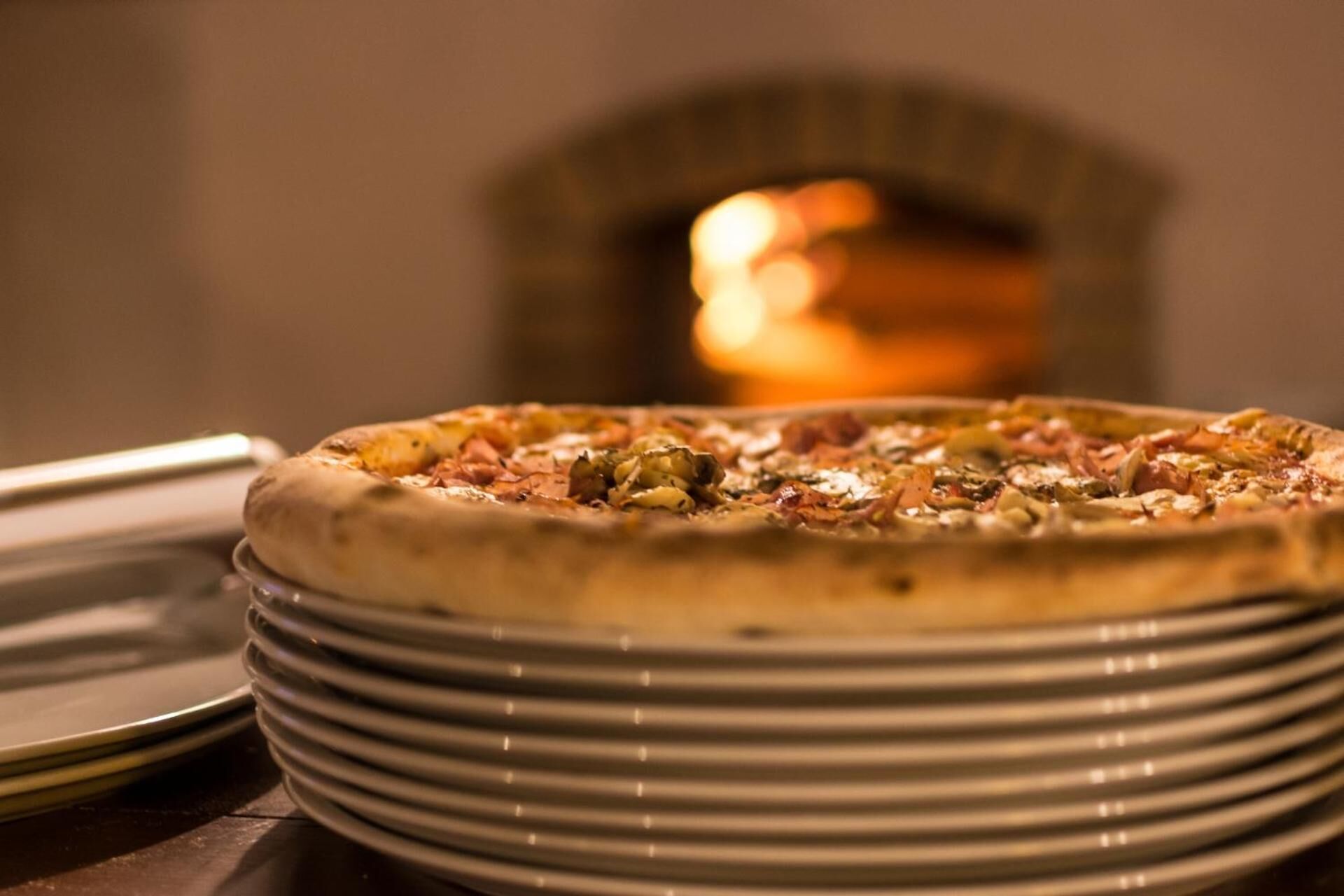 A pizza on a stack of plates with a blurred background of a fireplace.