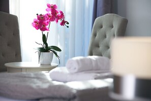 Una habitación de hotel con una cama, una mesita redonda con una orquídea en maceta y una silla.