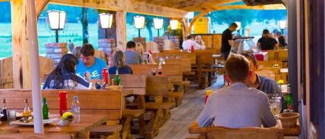 An outdoor restaurant with wooden tables and benches, covered by a yellow canopy with the brand name visible.