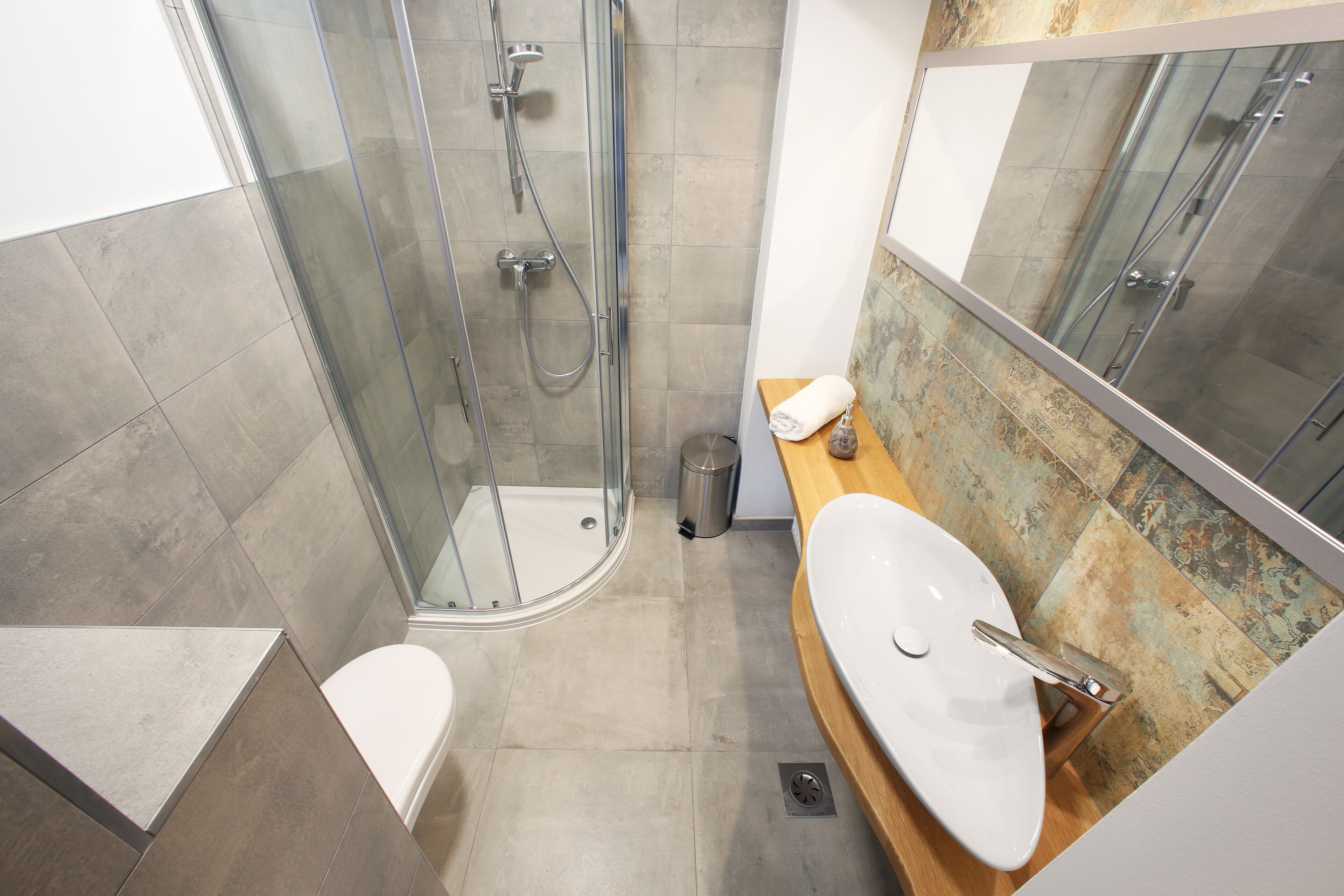 A modern bathroom with a glass shower enclosure, a white toilet, and a wooden vanity with a sink.