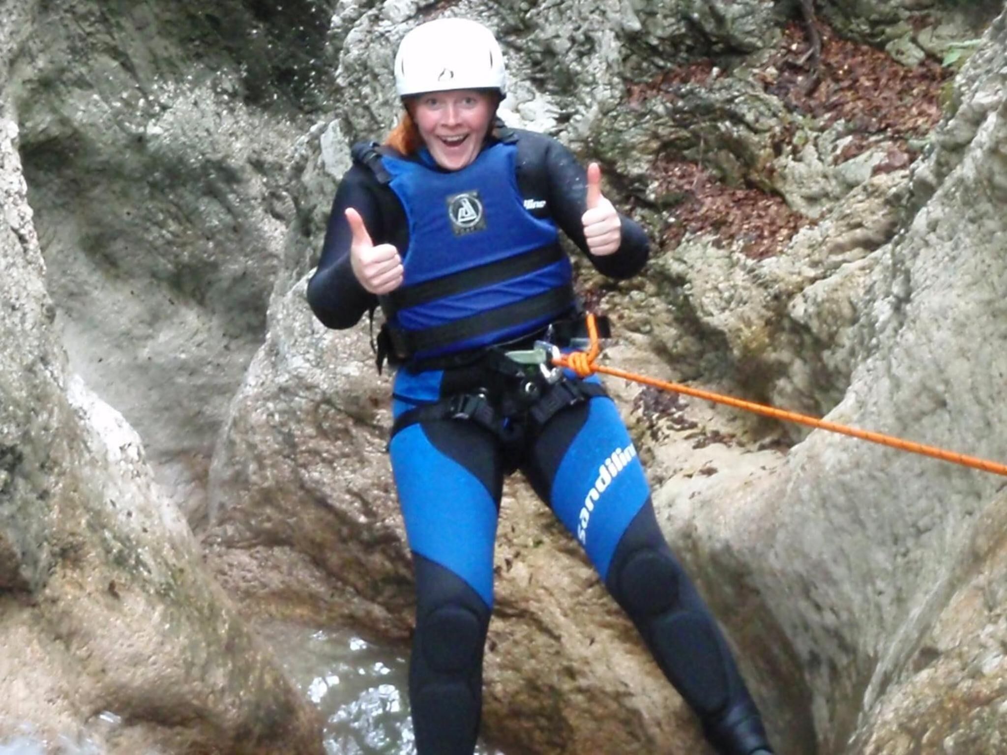 A person bungee jumping with a harness and helmet, surrounded by rocky terrain and water.