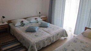 A bedroom with a large bed, a smaller bed, a nightstand, a lamp, and a window with curtains. - Apartments Biocic (Korcula)