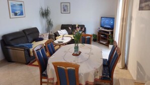 A living room with a sofa, a dining table with chairs, a TV, and a plant. - Apartments Biocic (Korcula)