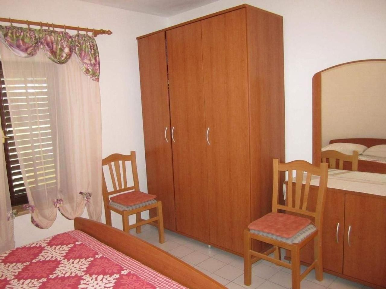 Une chambre à coucher avec un lit, deux chaises en bois, une armoire et une fenêtre avec des rideaux.
