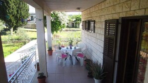 A covered outdoor patio with a table and chairs, potted plants, and a view of the surrounding garden. - Apartments Biocic (Korcula)