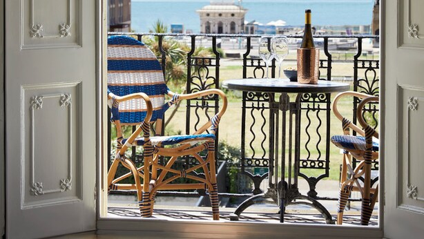 A balcony with wicker chairs and a table, overlooking a coastal view with buildings and the sea. - Artist Residence Brighton (Brighton)