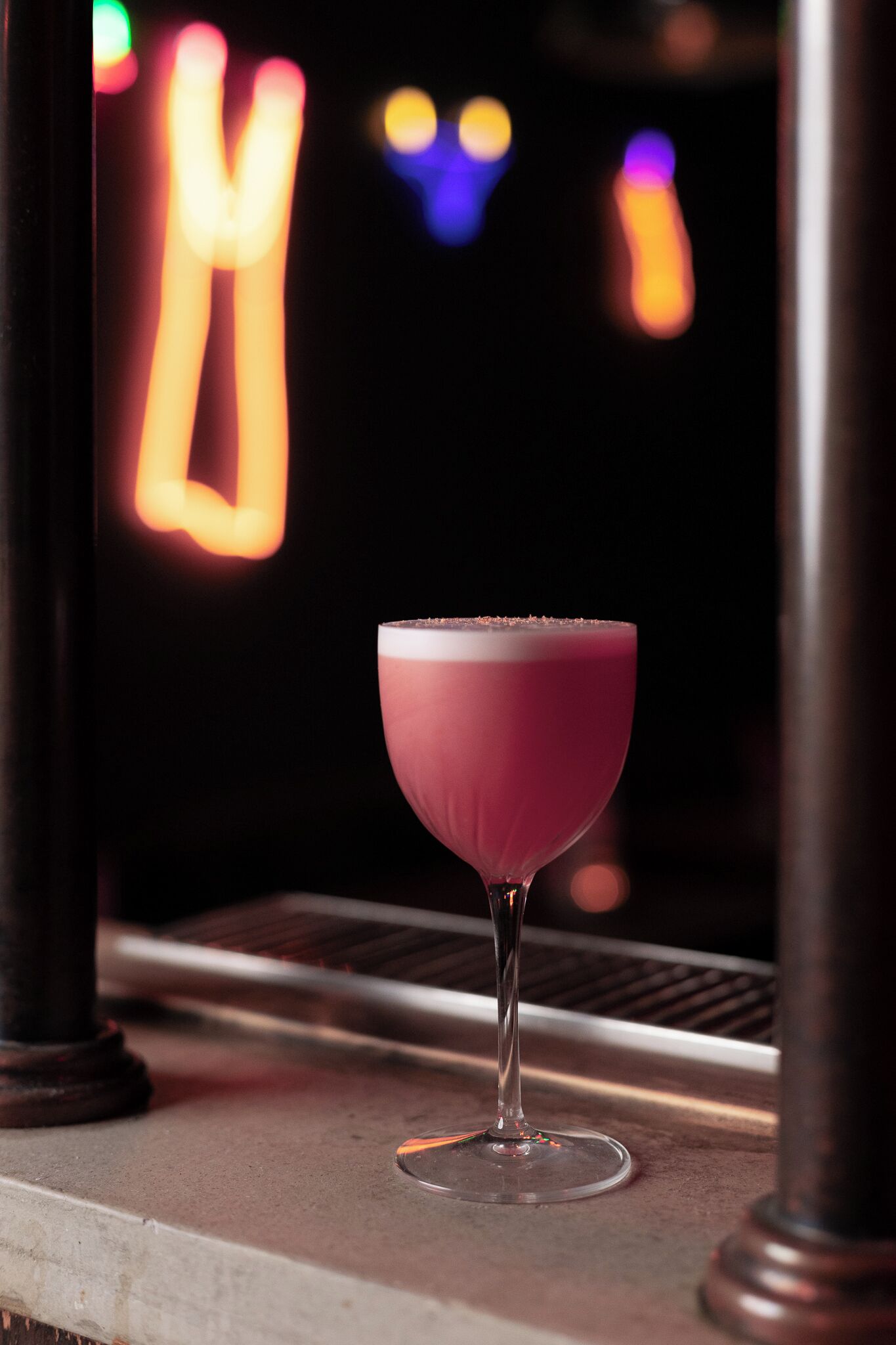 A cocktail glass on a bar counter with blurred colorful lights in the background.