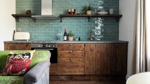 A kitchen with teal tiles, wooden cabinets, a built-in oven, and a countertop with a toaster and wine bottle. - Artist Residence Brighton (Brighton)