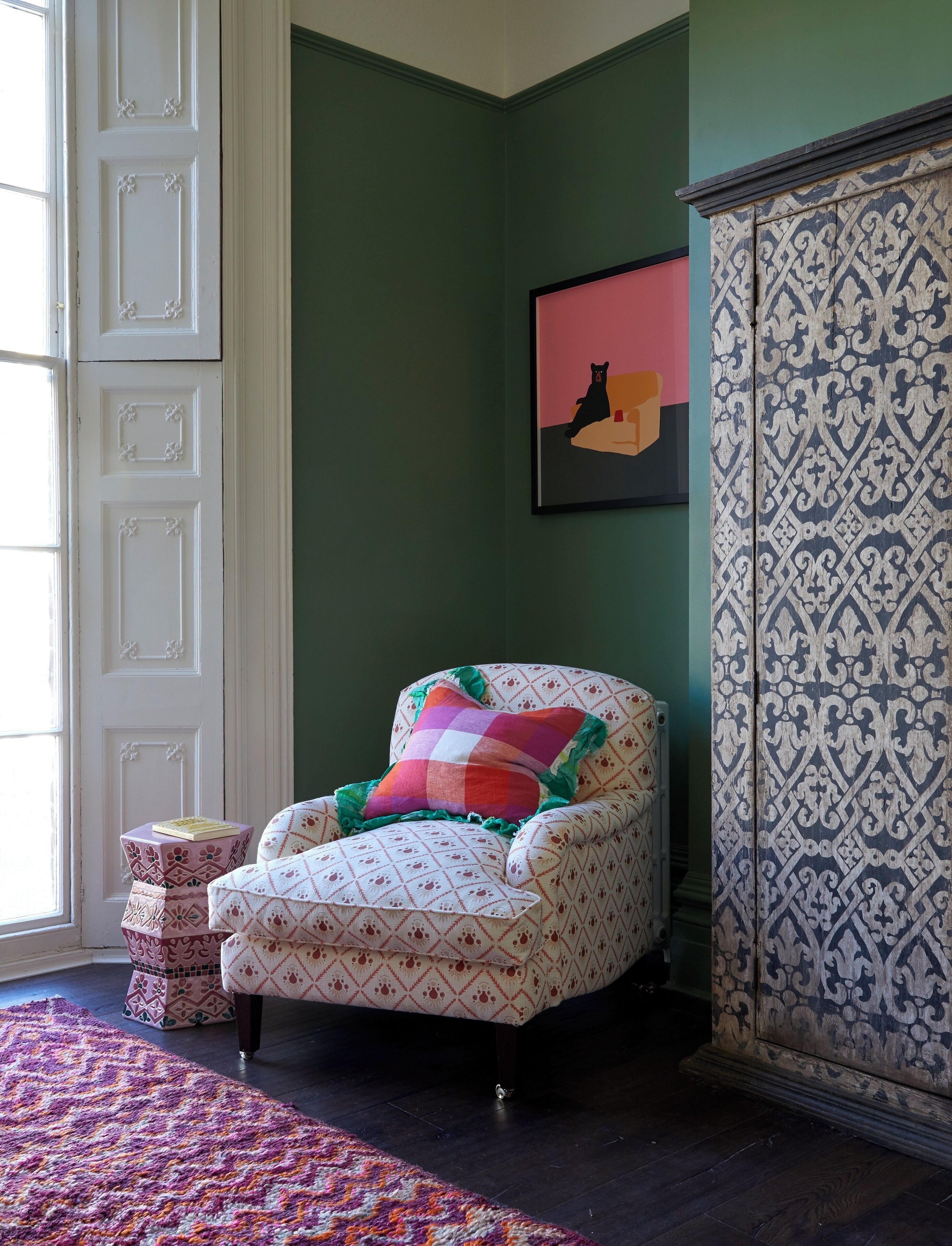 Um quarto com uma poltrona estampada, uma mesinha lateral, um armário estampado e uma obra de arte emoldurada na parede.