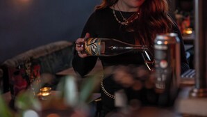 A person pouring a drink into a glass at a bar with string lights in the background. - Artist Residence Brighton (Brighton)