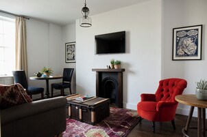Una sala de estar con chimenea, televisor montado en la pared y un sillón rojo.