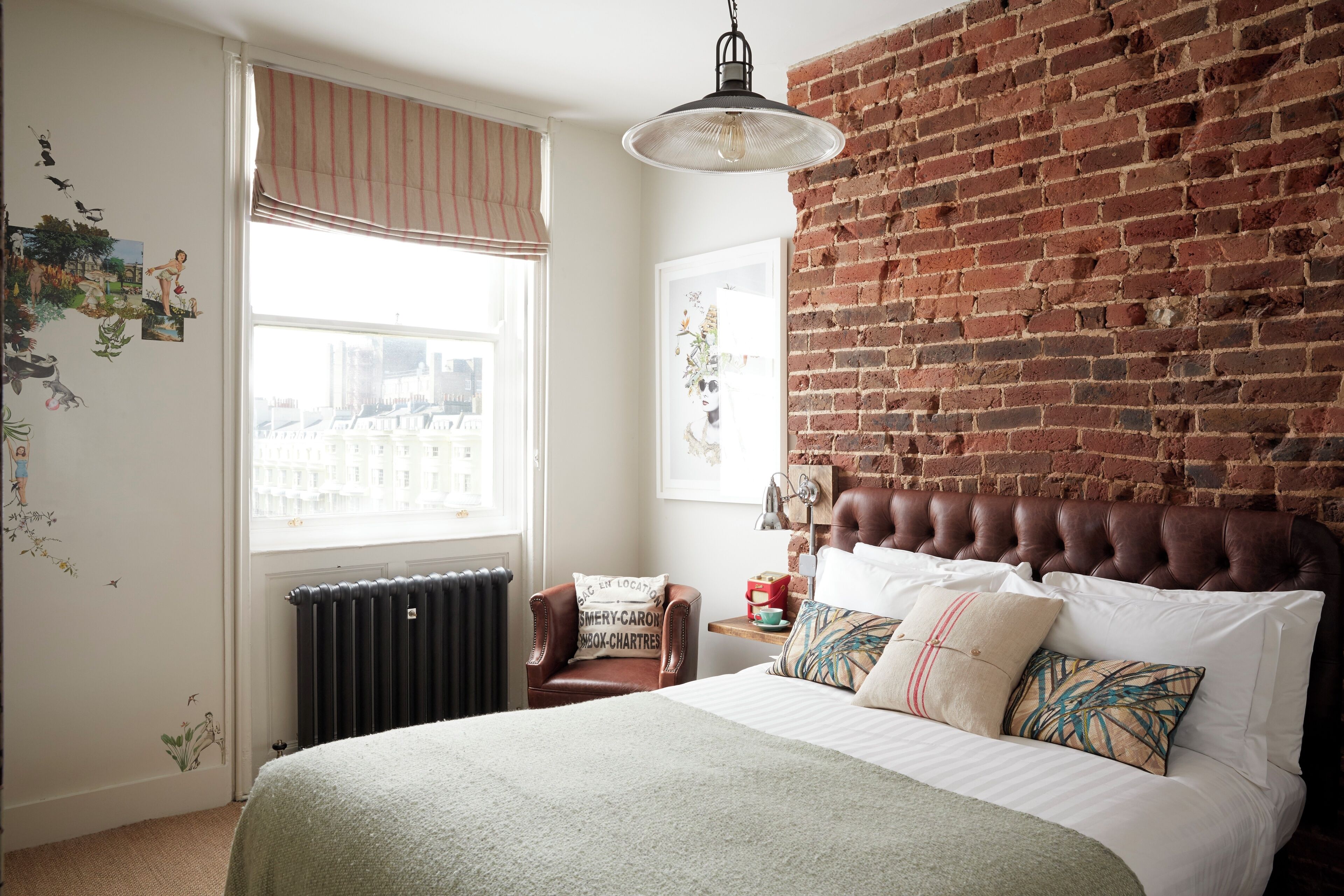 Un dormitorio con pared de ladrillo, una cama grande, una ventana con persianas, un radiador y una silla con cojín.
