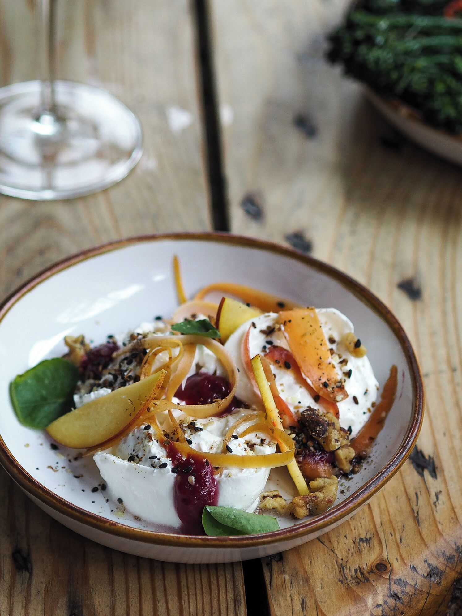 A dessert plate with poached eggs, fruit, and nuts on a wooden table.