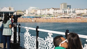 A coastal promenade with a white ornate railing, a beach in the background, and a cityscape with buildings. - Artist Residence Brighton (Brighton)