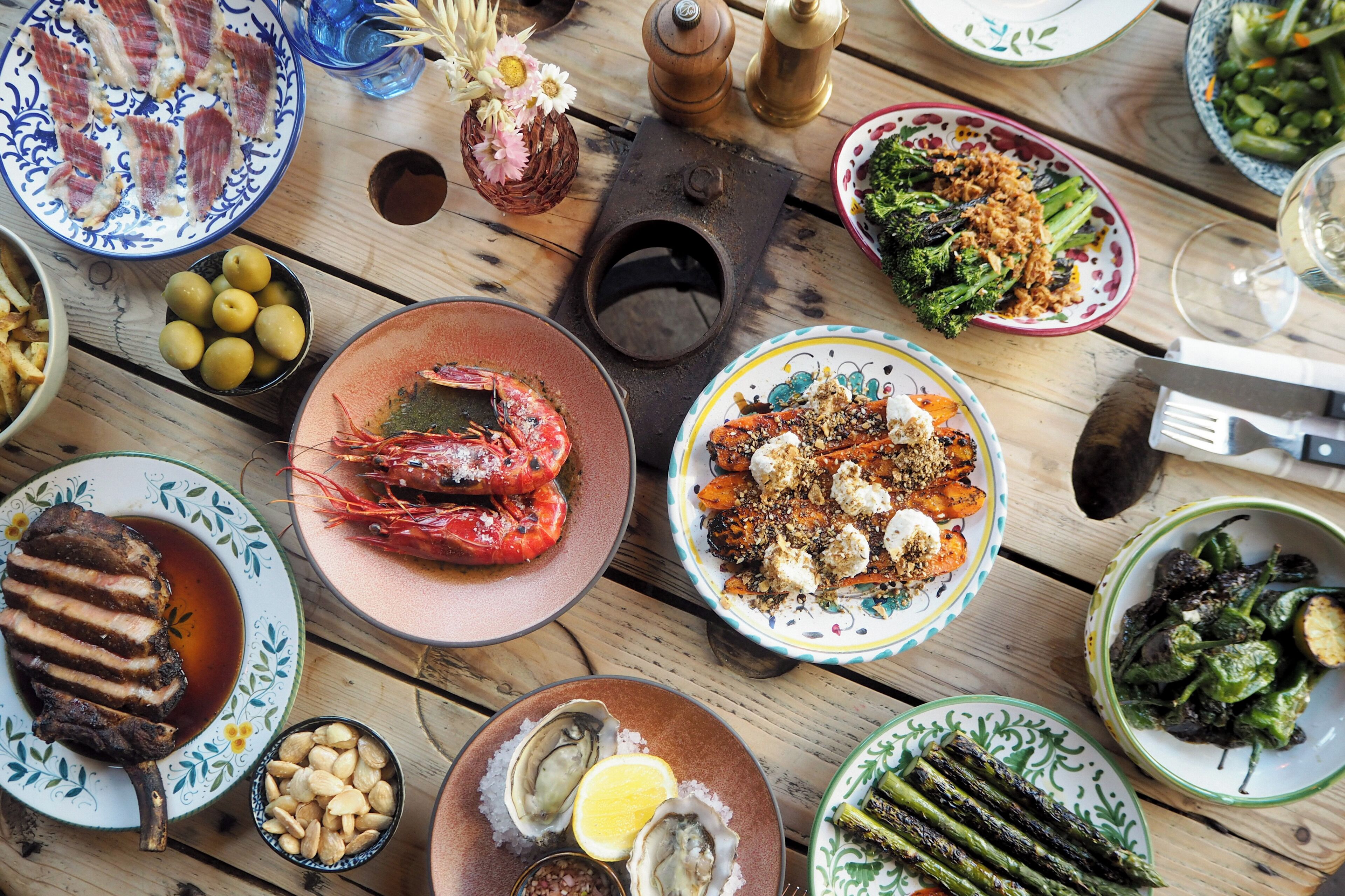 Una mesa de madera con diversos platos, incluyendo mariscos, verduras y un bistec.