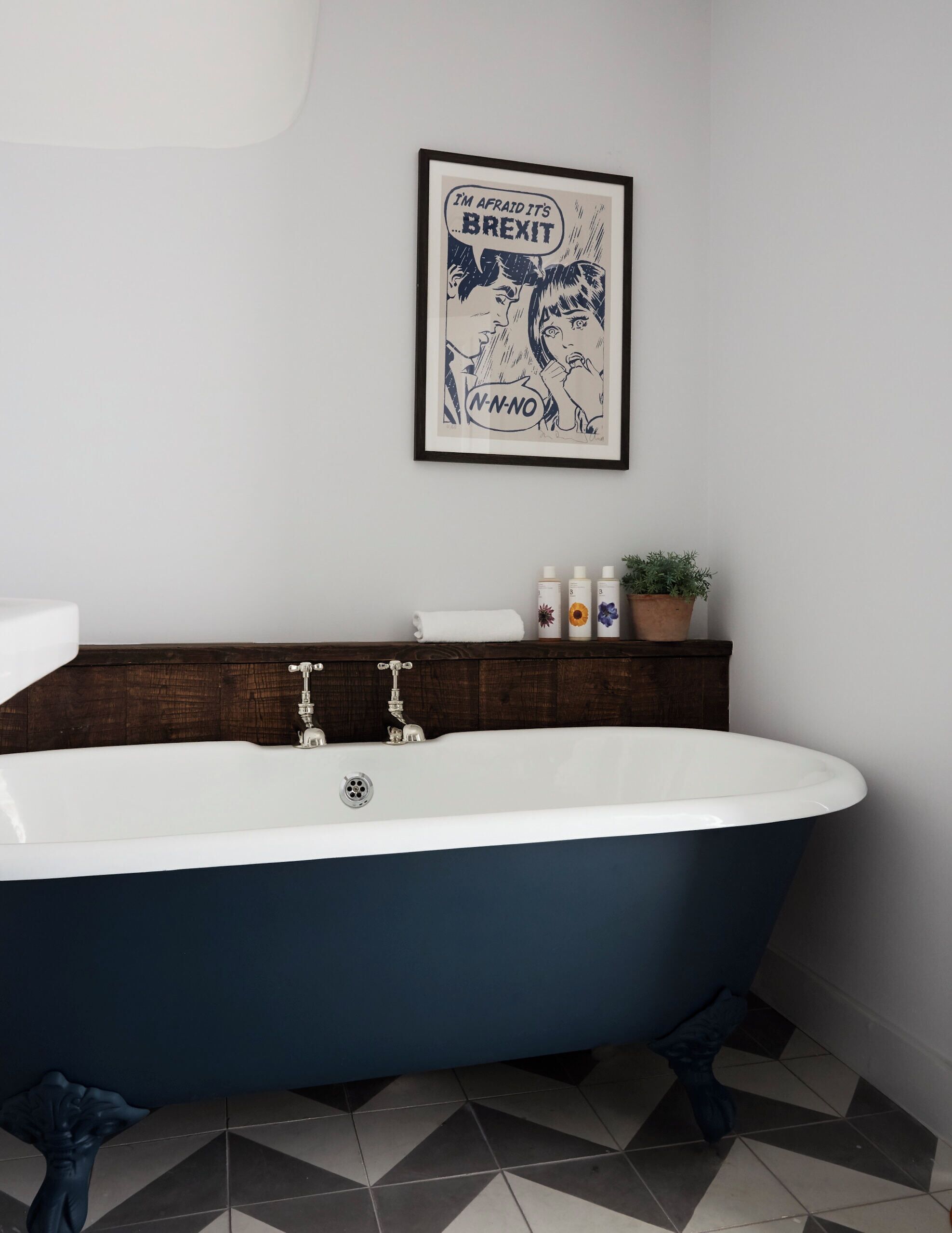 A bathroom with a freestanding bathtub, a wooden shelf with toiletries, and a framed picture on the wall.