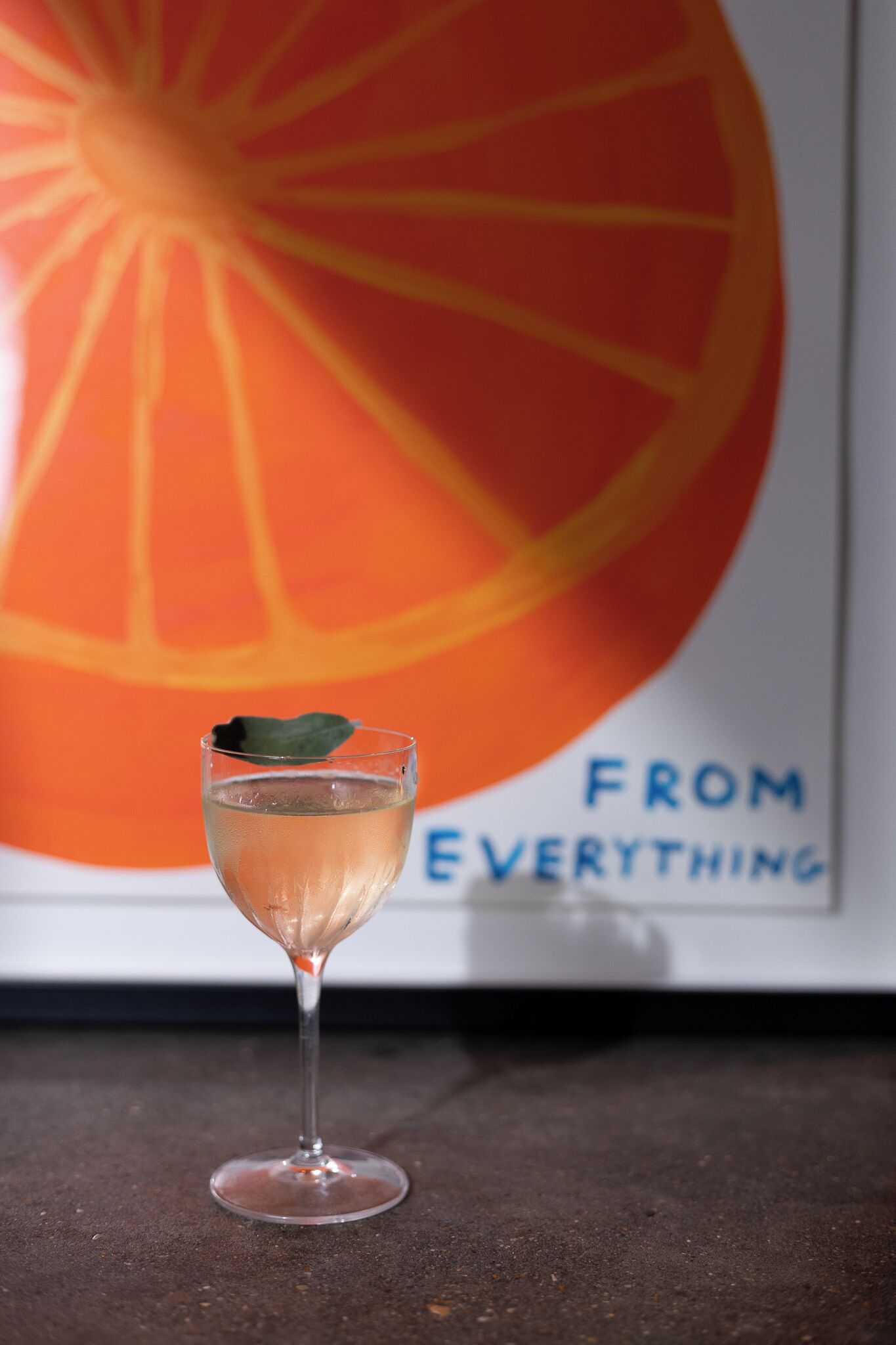 A cocktail glass with a leaf garnish on a dark surface, with a large orange slice and the text "FROM EVERYTHING" in the background.