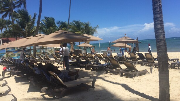 Une plage avec des chaises longues et des parasols, des palmiers et un ciel bleu azur.