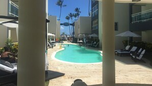 Un espace piscine doté de chaises longues et de parasols, entouré de bâtiments et de palmiers.