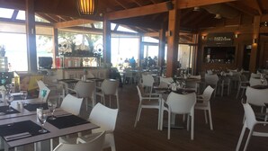 Un restaurant avec des poutres en bois, des chaises en plastique blanc et des tables dressées pour le service.