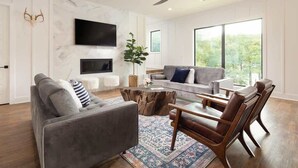 Een moderne woonkamer met een bank, salontafel en stoelen, een flatscreen televisie en een groot raam met uitzicht.