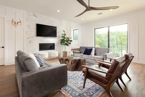 A modern living room with a sofa, coffee table, and chairs, a flat-screen TV, and a large window with a view.