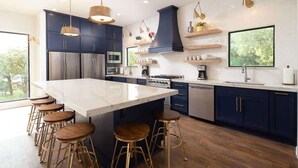 Een moderne keuken met een centraal eiland, barkrukken, roestvrijstalen apparatuur en houten vloeren.