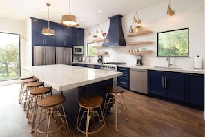 A modern kitchen with a central island, bar stools, stainless steel appliances, and wooden flooring.