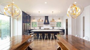 Een moderne keuken met een centraal eiland, barkrukken, hanglampen en uitzicht op de omgeving.