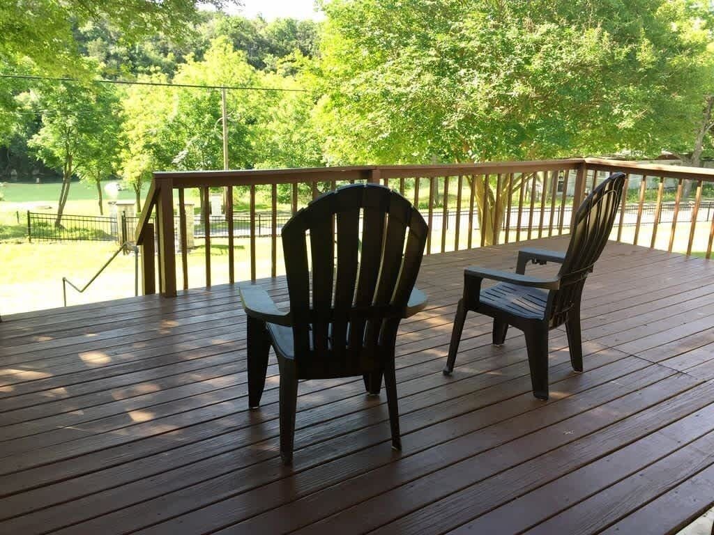 Une terrasse en bois avec deux fauteuils Adirondack et une table, donnant sur une étendue d’eau et des arbres.