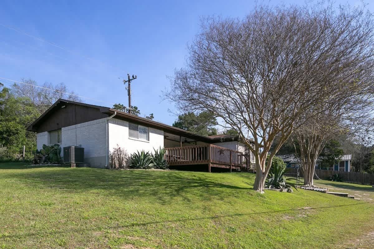 Una casa de un nivel con patio cercado, terraza de madera y un árbol grande.
