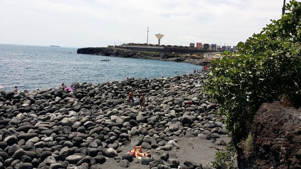 A rocky beach with people sunbathing and swimming, a distant cityscape, and a large water tower.