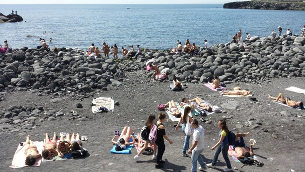 Una playa con gente tomando el sol y nadando.