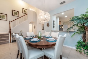 Enjoy meals in this dining area with a round table for four, a staircase, and a kitchen in the background.