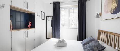A hotel room with a bed, a wardrobe, a window with curtains, and a wall-mounted lamp.