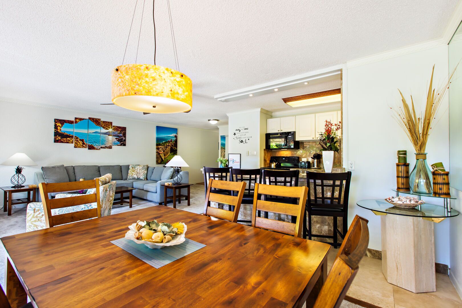 A modern living room with a wooden dining table, a sofa, and a kitchen area visible through an open door.