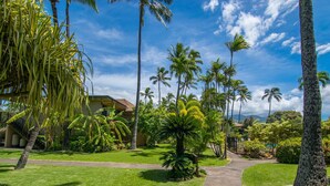 A tropical garden with a pathway leading to a building with a balcony. - Oceanfront 2bd, lanai with Kaanapali pool views (Lahaina)