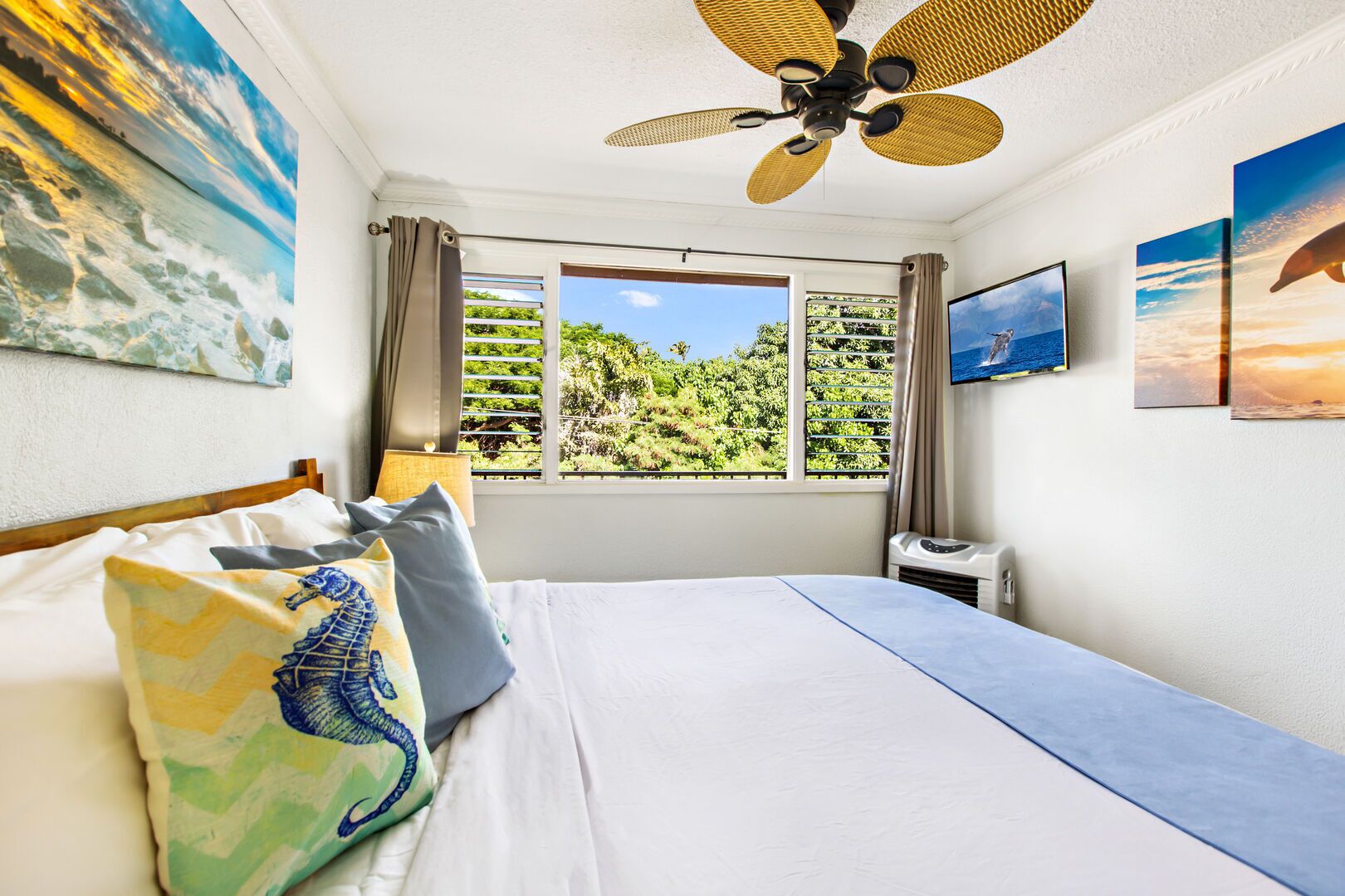 Une chambre d’hôtel avec un lit, un ventilateur de plafond, une fenêtre donnant sur un paysage verdoyant et un téléviseur fixé au mur.
