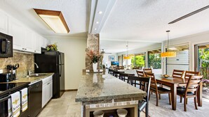 A modern kitchen with granite countertops, stainless steel appliances, and a dining area with wooden chairs and a large table. - Oceanfront 2bd, lanai with Kaanapali pool views (Lahaina)