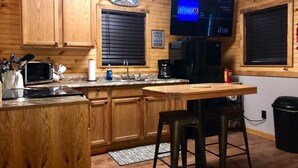 Una cocina con armarios de madera, microondas, cafetera, fregadero y un televisor montado en la pared.