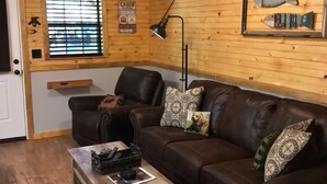Una habitación acogedora de estilo cabaña con un sofá de cuero marrón, una mesa de centro de madera y una lámpara.