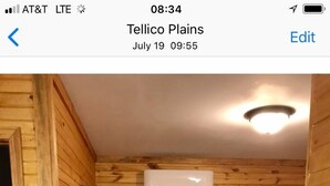 Una habitación acogedora con detalles de madera, una cama con ropa de cama a cuadros, una mesita de noche, una lámpara y un equipo de aire acondicionado.
