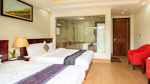Ein Hotelzimmer mit zwei Betten, einem roten Sessel, Holzdielen und einem großen Fenster.