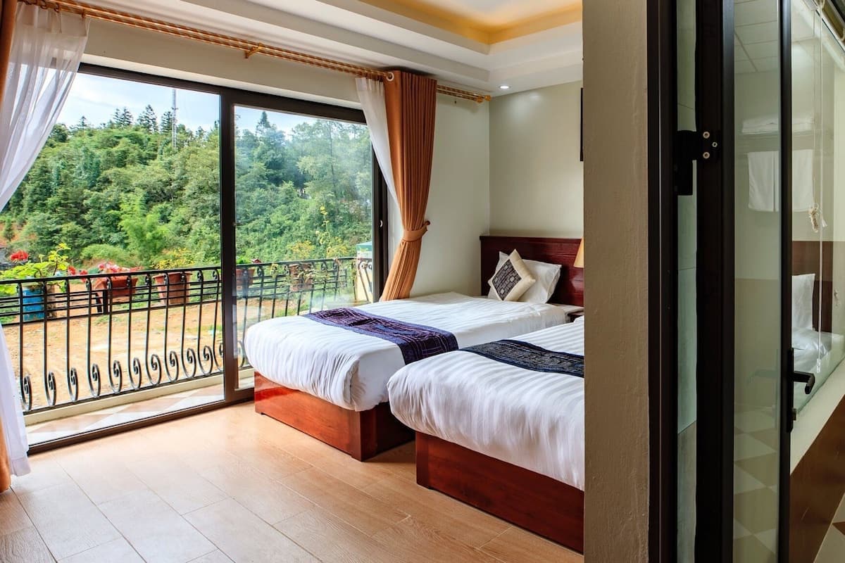 Ein Hotelzimmer mit zwei Betten, einem Balkon mit Blick auf Grünflächen und einer Duschkabine aus Glas.