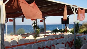 An outdoor dining area with white chairs and red sashes, overlooking the sea. - Lasia Hotel (Lesvos)