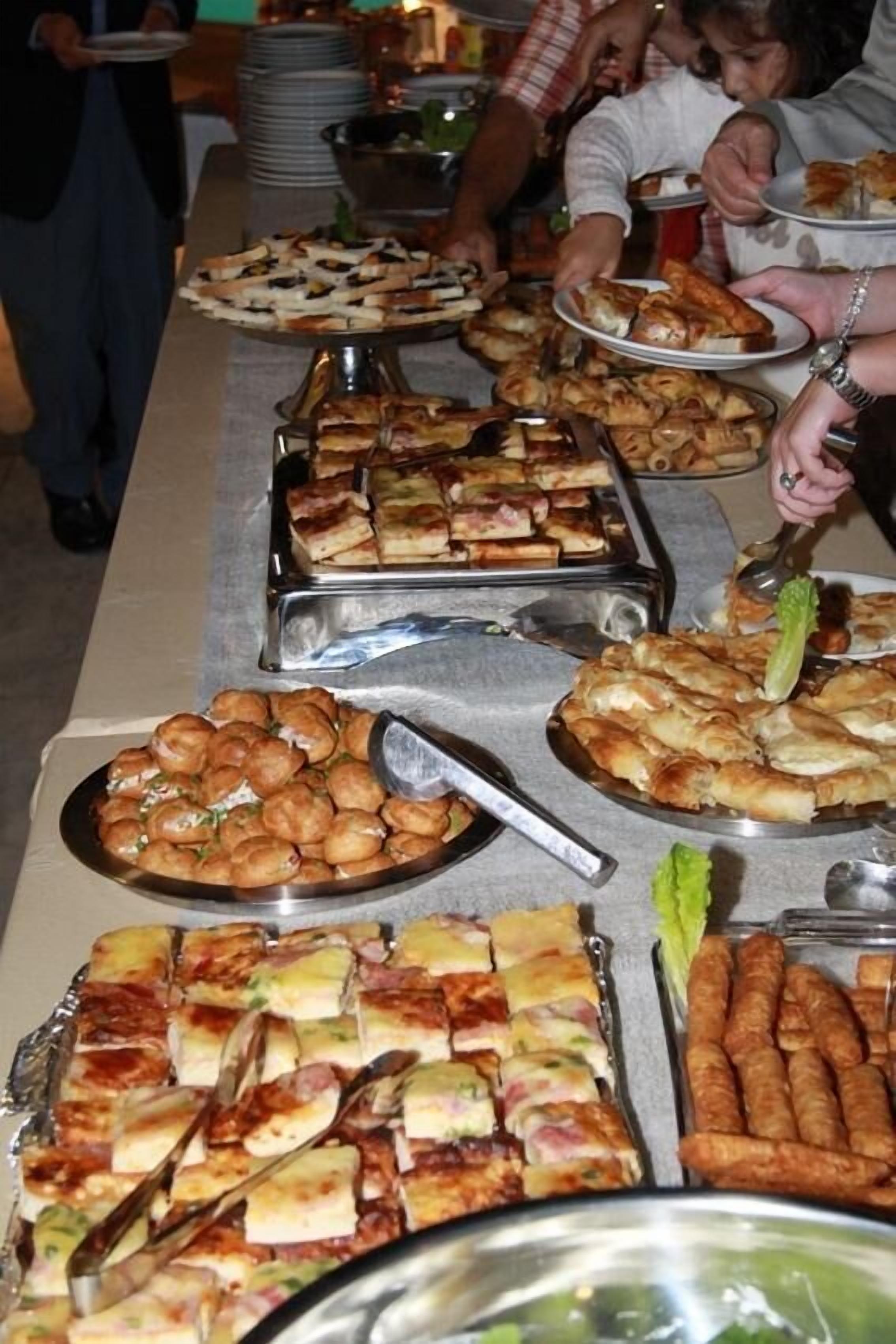 Un bufet ben carregat amb diferents plats, incloent pizzes, pastissos i altres menjars.