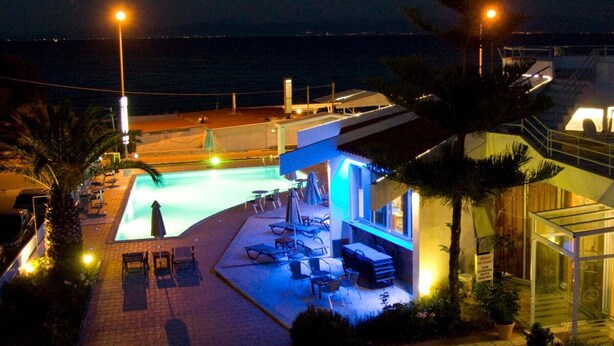 A nighttime view of a hotel with a swimming pool, outdoor seating area, and a view of the sea. - Lasia Hotel (Lesvos)