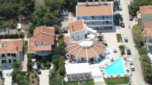 An aerial view of a hotel with a central pool, multiple buildings, and a road in the foreground. - Lasia Hotel (Lesvos)