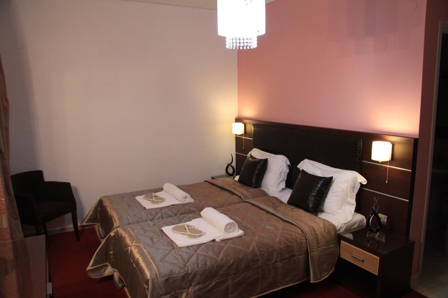 A hotel room with a bed, nightstands, a chair, and a chandelier.